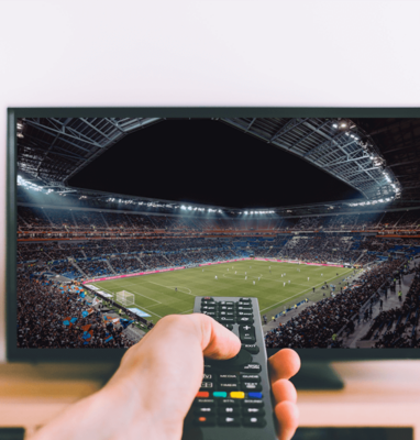 Hand with a remote control watching a football match in a stadium on TV