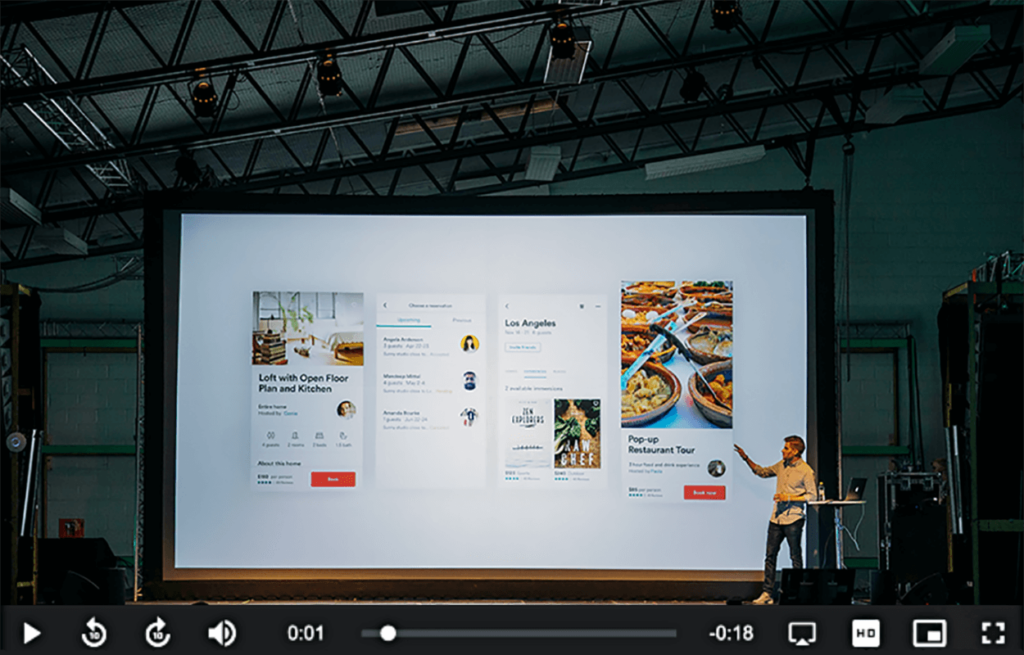 Presenter on stage beside a large screen video player, video for engagement