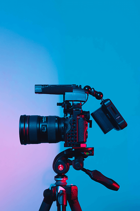 Video camera on a tripod against a blue background, illustrating live stream contribution from studios